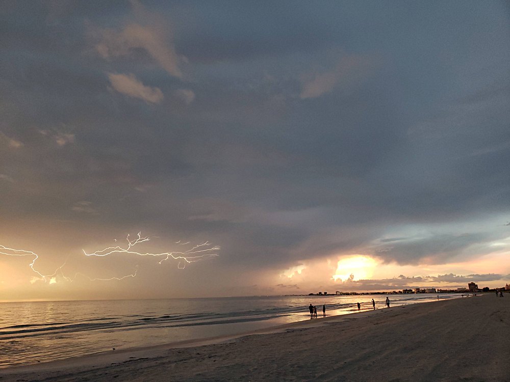 Branching lightning striking off the coast of a beach at sunset