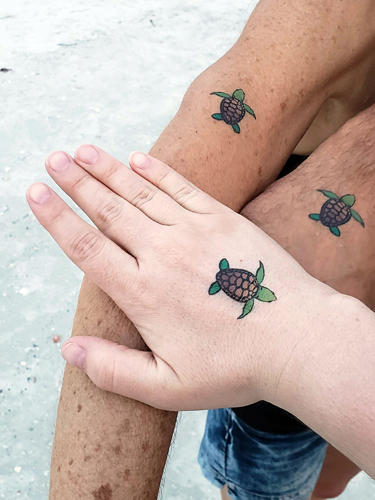 The arms/hands of three people, all displaying the same temporary sea turtle tattoo