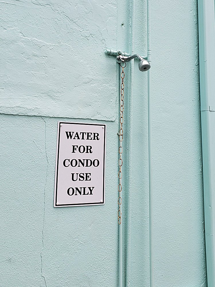 An outdoor shower faucet with a sign declaring 'water for condo use only'